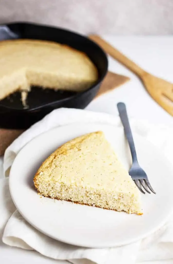 A slice of Southern Cornbread with iron skillet in back ground