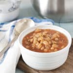 A photo of a bowl of baked beans with a silver pot in the background for How to Cook Canned Baked Beans