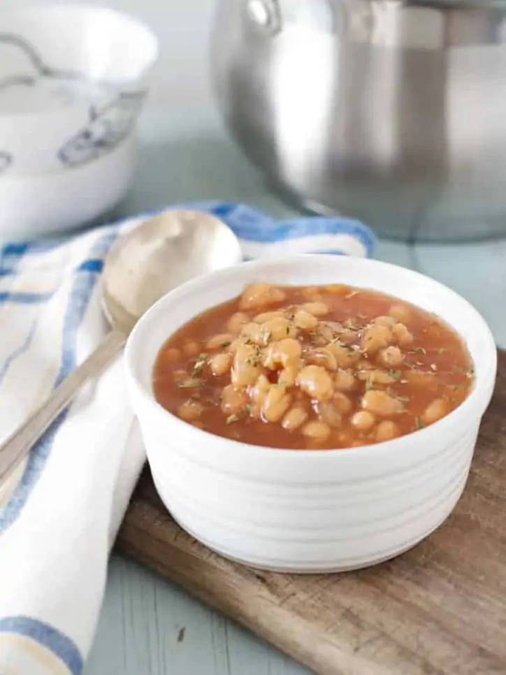 A photo of a bowl of baked beans with a silver pot in the background for How to Cook Canned Baked Beans