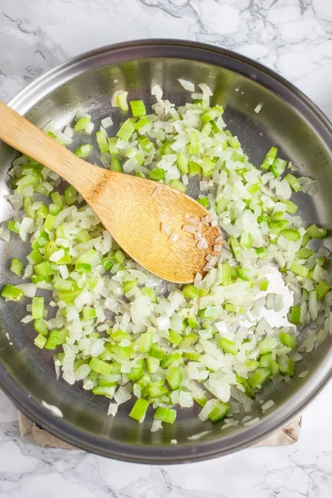 A photo of celery and onions in a skillet on marble table