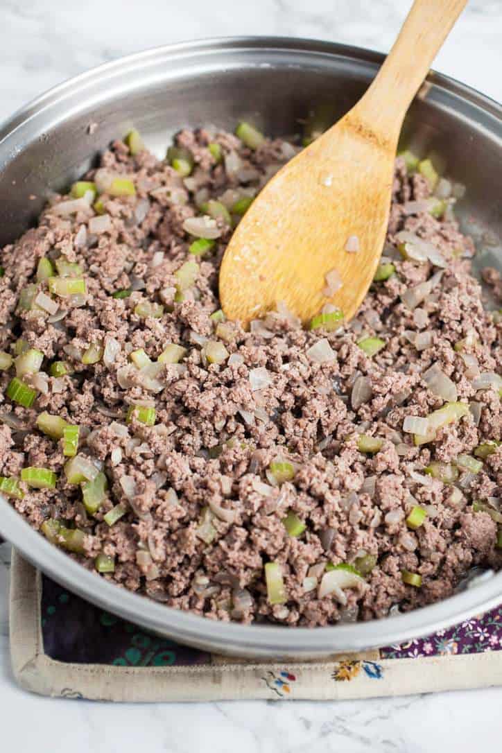 A skillet of burger with celery and onions on a hot pad