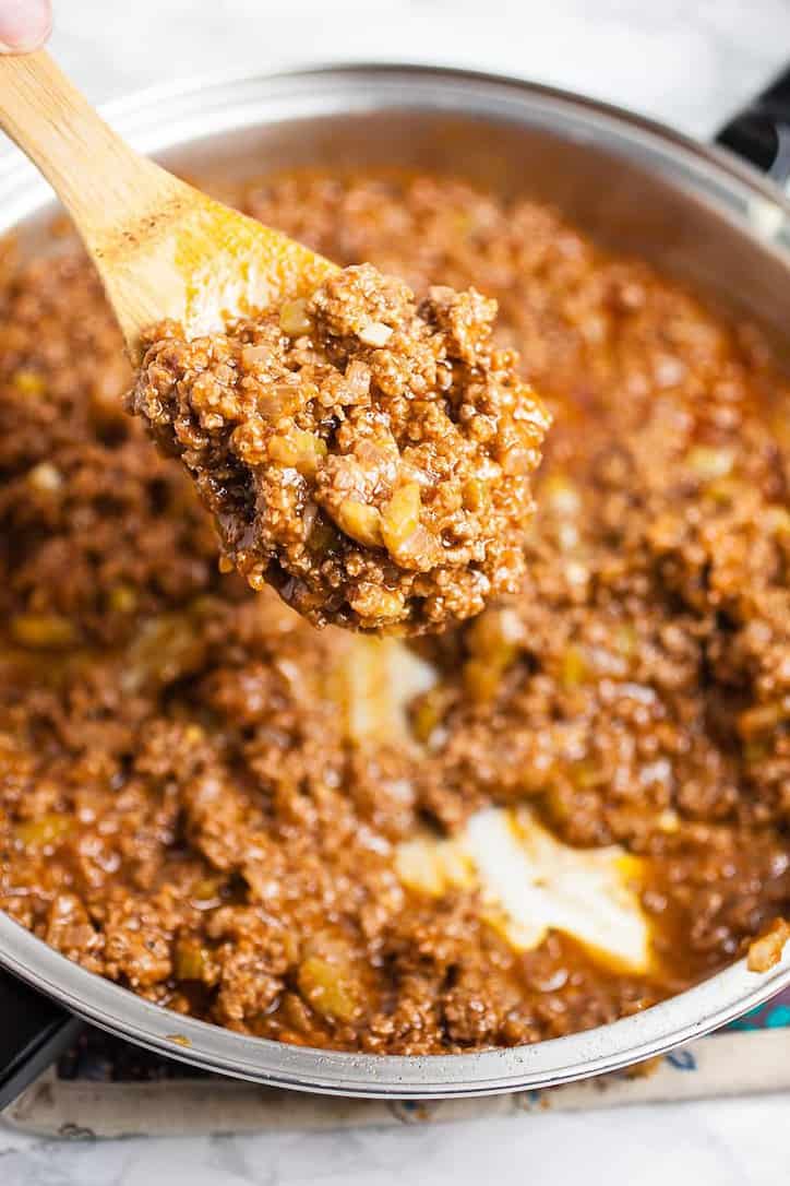 A frying pan of sloppy joes ground beef with wooden spoon lifting some out of the pan