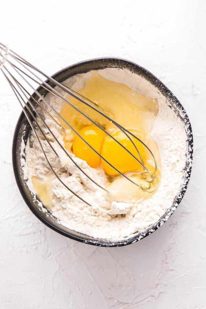 bowl of flours and eggs with whisk