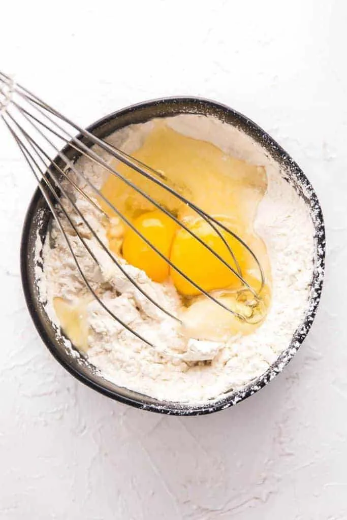 bowl of flours and eggs with whisk