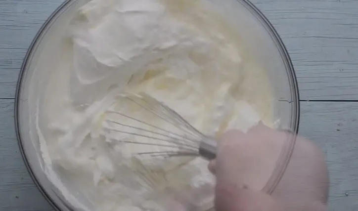 a glass bowl with cool whip, sour cream and milk and whisk