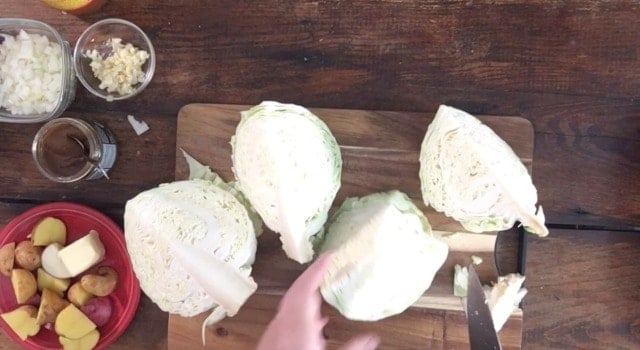 A cabbage head cut into fourths with cutting board and knife