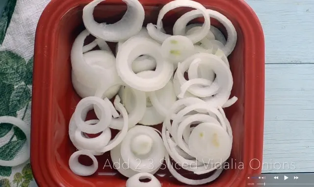 Red pan filled with vidalia onion slices, kitchen towel in background