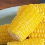 Close up photo of a glistening ear of corn sitting on other ears on a blue plate