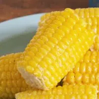 Close up photo of a glistening ear of corn sitting on other ears on a blue plate