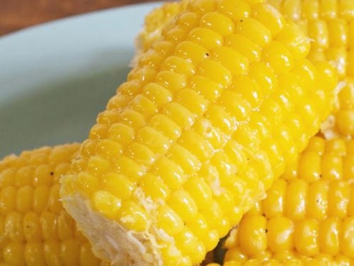 Close up photo of a glistening ear of corn sitting on other ears on a blue plate