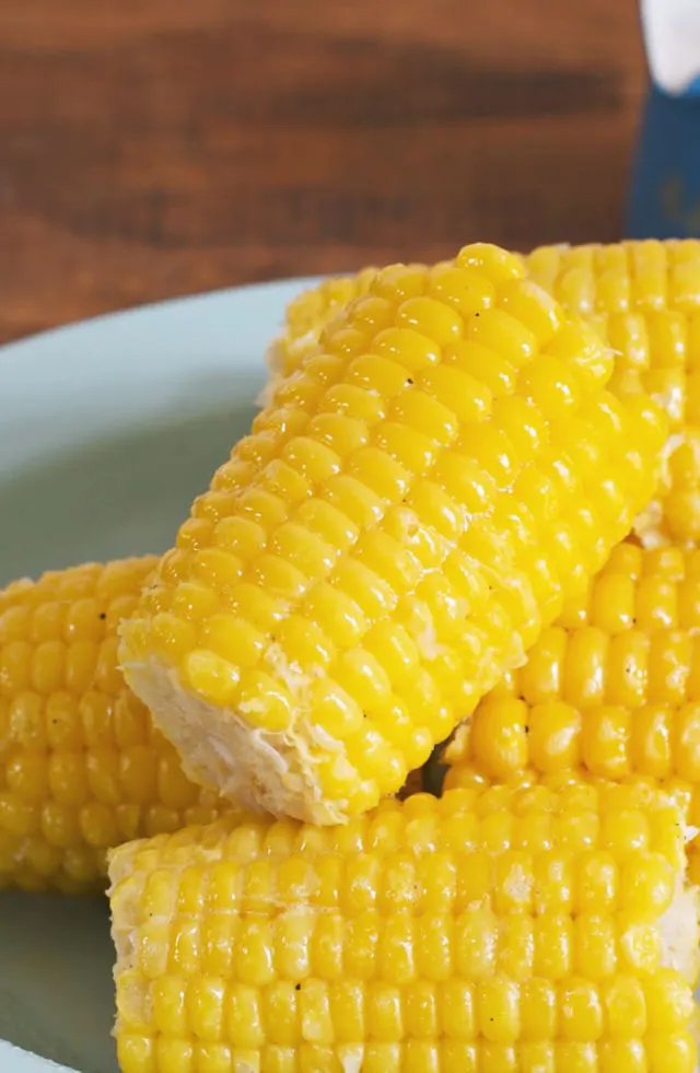 Close up photo of a glistening ear of corn sitting on other ears on a blue plate