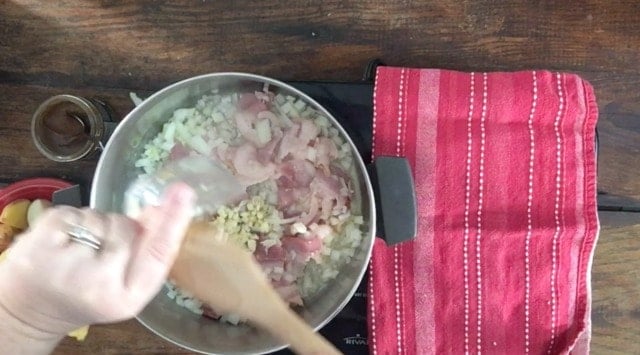 A stockpot with butter, bacon, onion and garlic in it. A red towel to the side