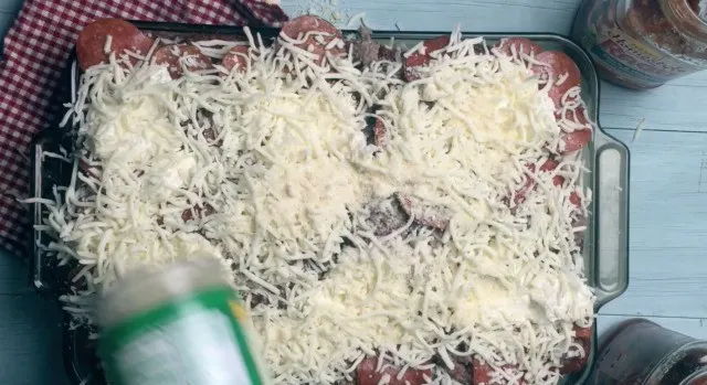 Parmesan Cheese being sprinkled on top of the 9x13 pan full of ingredients.