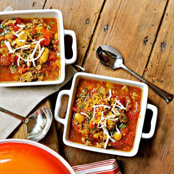 An overhead view of two square bowls of pinto bean soup recipe with a spoon on a wooden background