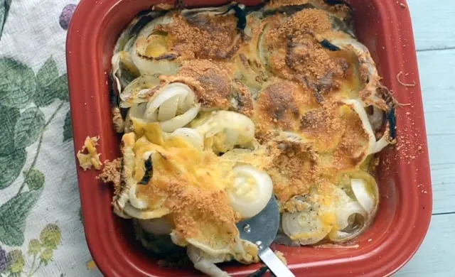 Red dish with baked onion casserole recipe being scooped out with silver spatula