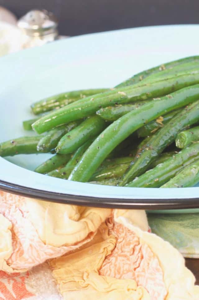 A close up of a plate of green beans sitting on an orange kitchen towel