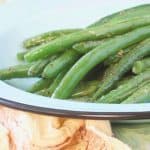 A close up of a plate of green beans sitting on an orange kitchen towel