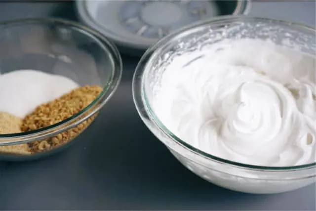 A bowl of whipped cream and another bowl of crushed crackers and peanuts