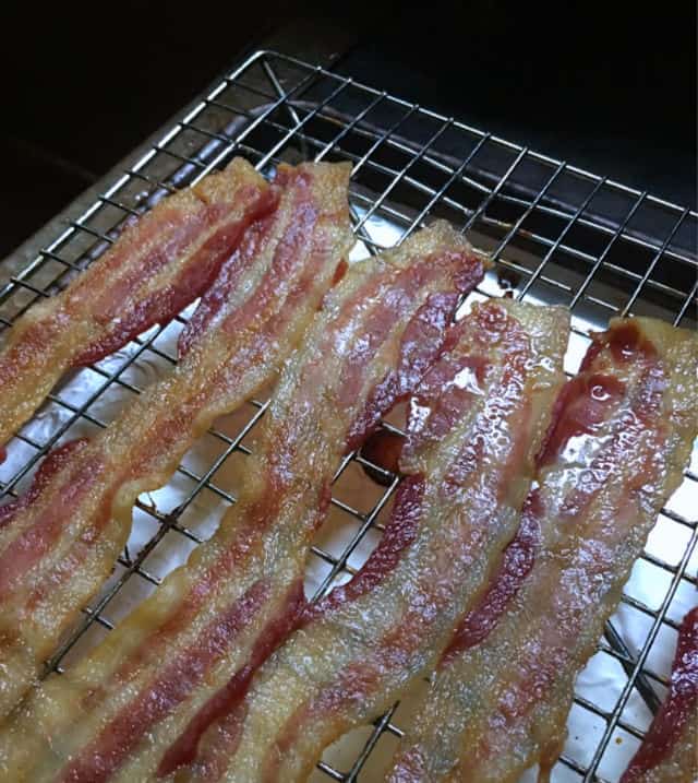  a photo of five strips of cooked bacon on a rack with grease glistening for How to Cook Bacon in the Oven on a Rack