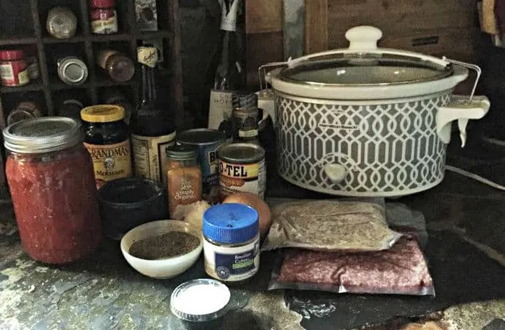 A clutter of mess on the kitchen counter with jars, packages and slow cooker.