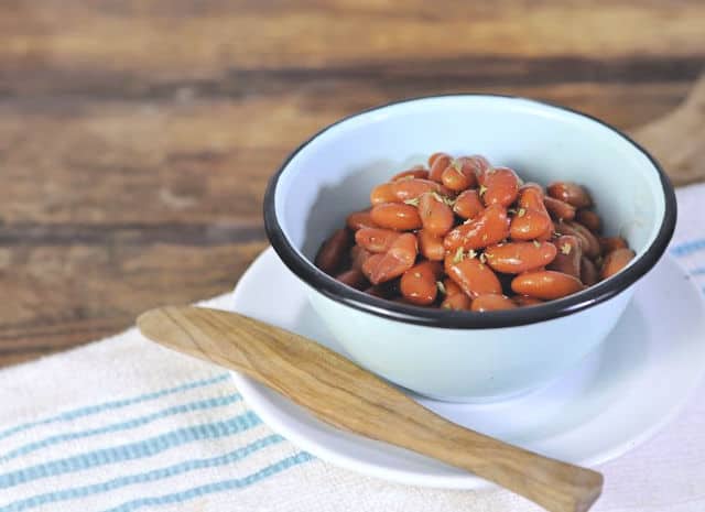 A small blue bowl of kidney beans sitting on a white plate with a wooden spatula