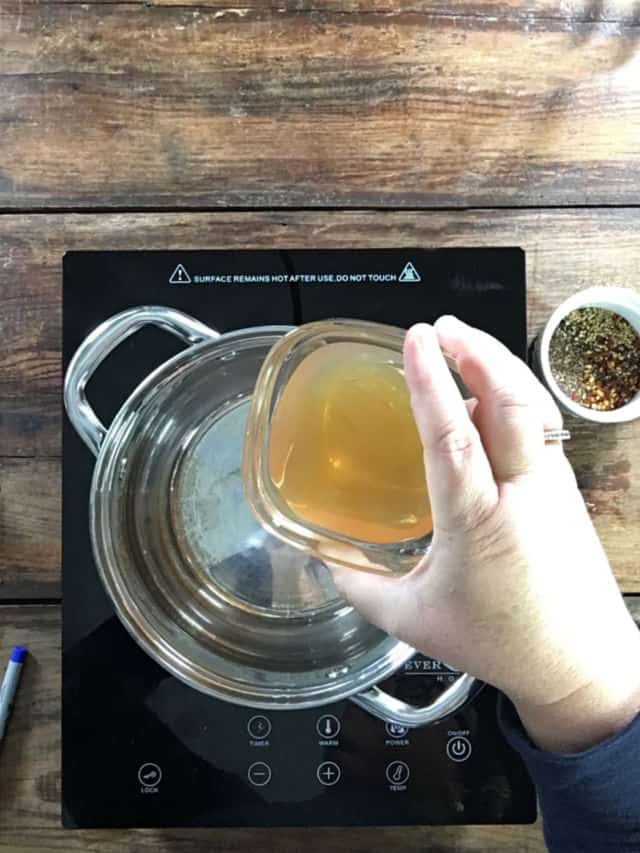 Adding the apple cider vinegar to the saucepan on the stove for Refrigerator Pickled Okra