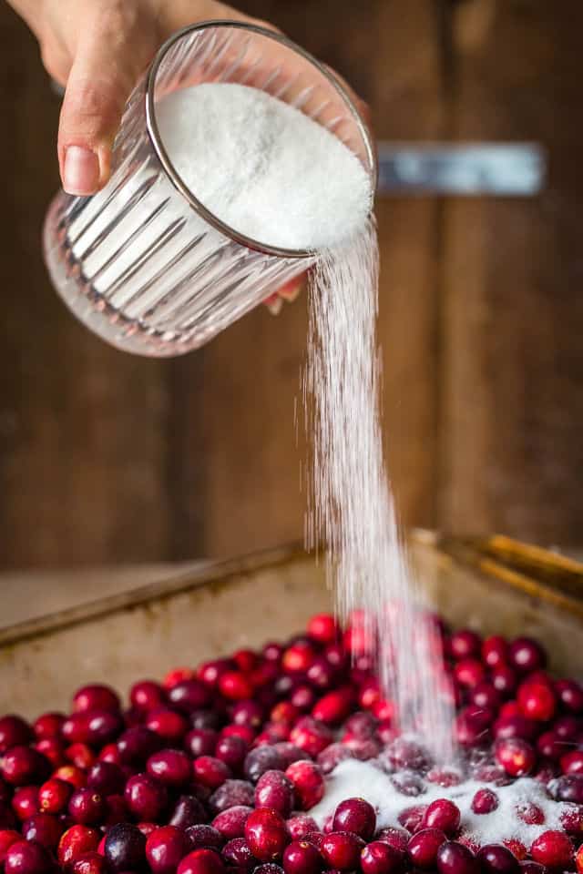 White sugar being poured over the cranberries in the pan