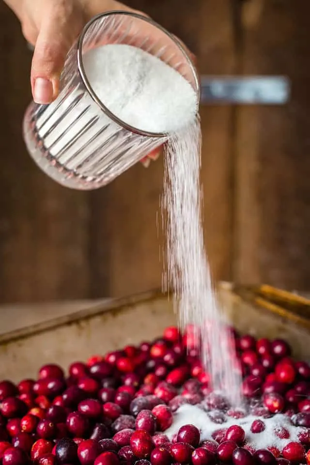 White sugar being poured over the cranberries in the pan