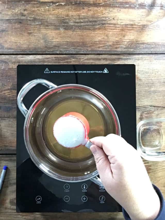 Adding the sugar to the saucepan of vinegar that is heating up for pickled blackberries