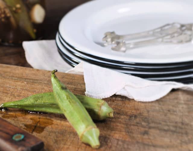 two okra pods and a stack of white plates with silver tongs