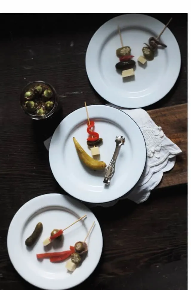 A diagonal line of three white plates with pickled okra and other appetizers 