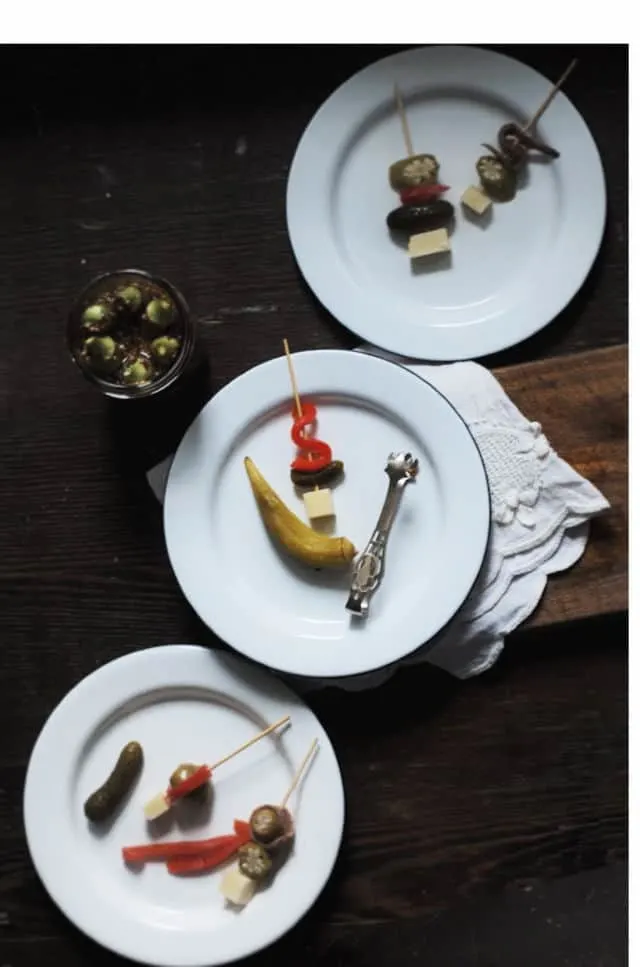 A diagonal line of three white plates with pickled okra and other appetizers
