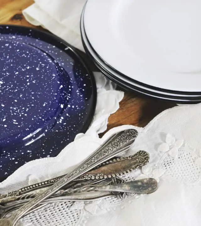 Stack of white plates with one upside down with blue speckled bottom and silverware