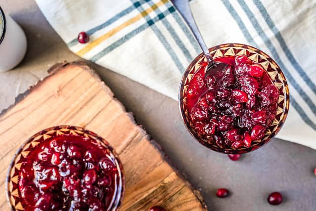 a close up of two goblets of completed cranberry sauce with a blue and yellow striped cloth napkin