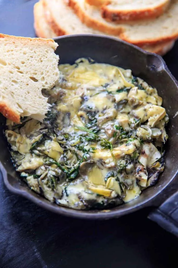 A skillet of the dip with a crusty piece of bread