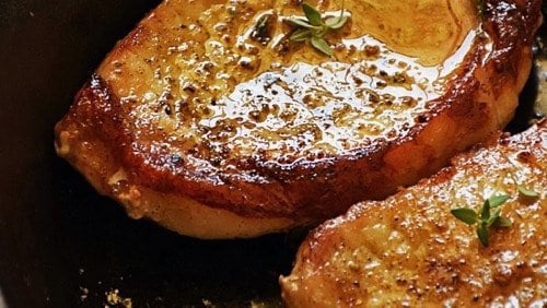 A close up photo of two pork chops with glistening grease on the top
