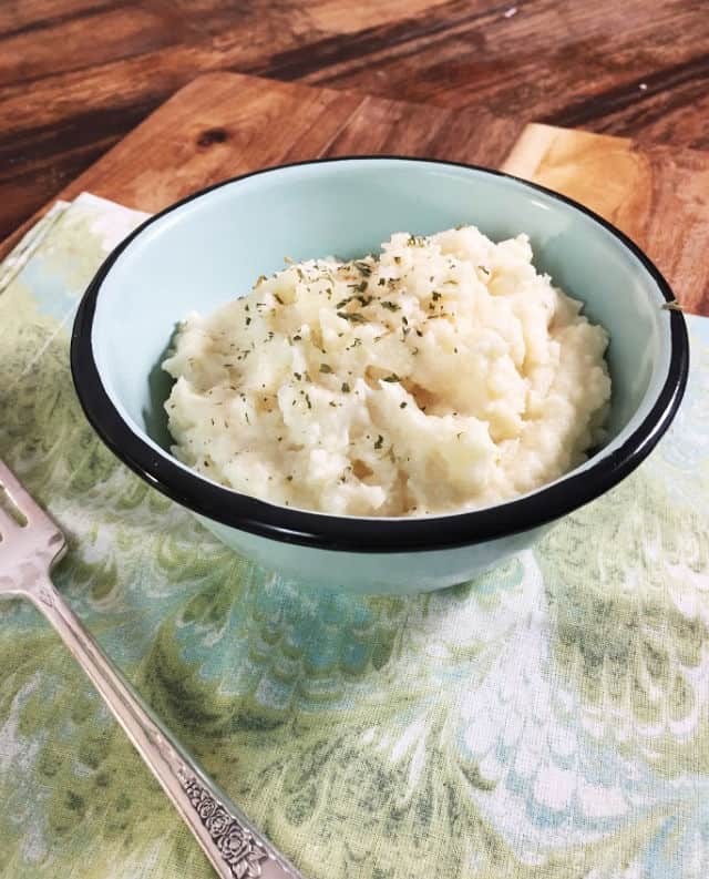 A bowl of mashed potatoes on a swirled green napkin and a fork