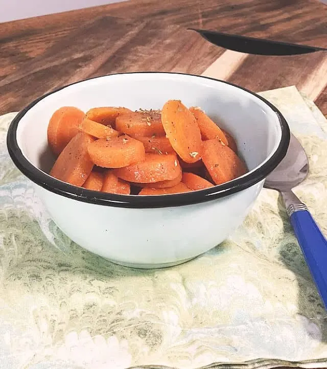 A bowl of carrots on a green napkin with blue spoon