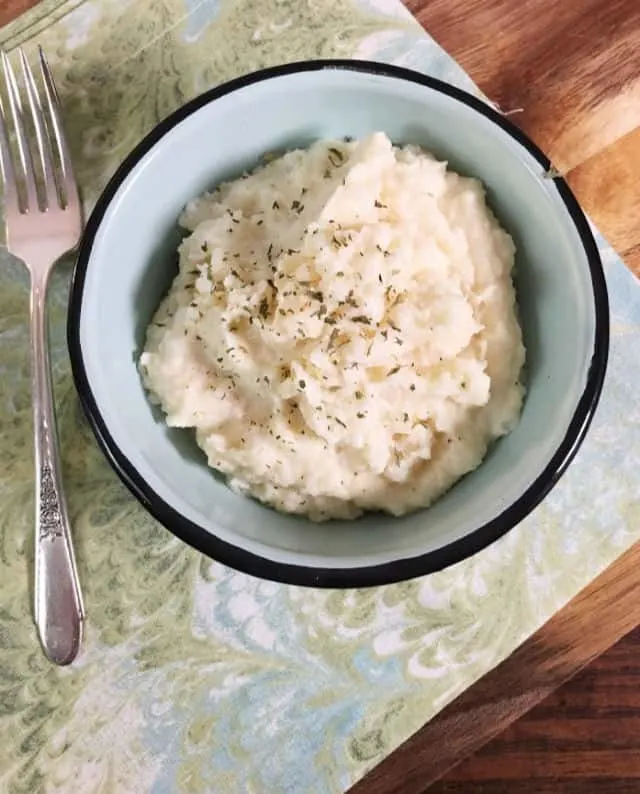 A bowl of instant mashed potatoes from above with a swirled green napikin and a fork using canned mashed potatoes
