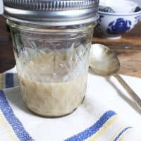 A jelly jar half full of bacon grease on a blue and white napkin