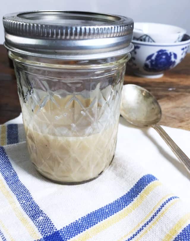 A jelly jar half full of bacon grease on a blue and white napkin