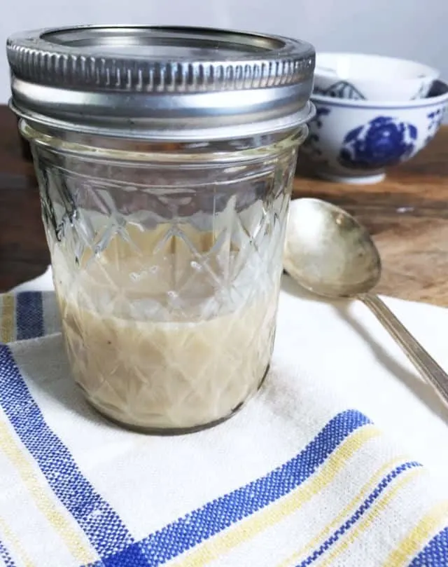 A jelly jar half full of bacon grease on a blue and white napkin