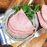 A view of three slices of ham on a grey plate with a blue napkin