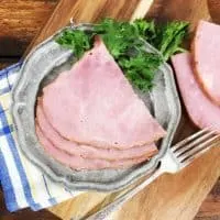 A view of three slices of ham on a grey plate with a blue napkin