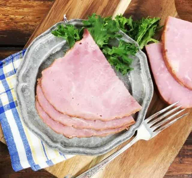 A view of three slices of ham on a grey plate with a blue napkin