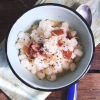 A bowl of hominy with blue handled spoon on green napkin from above