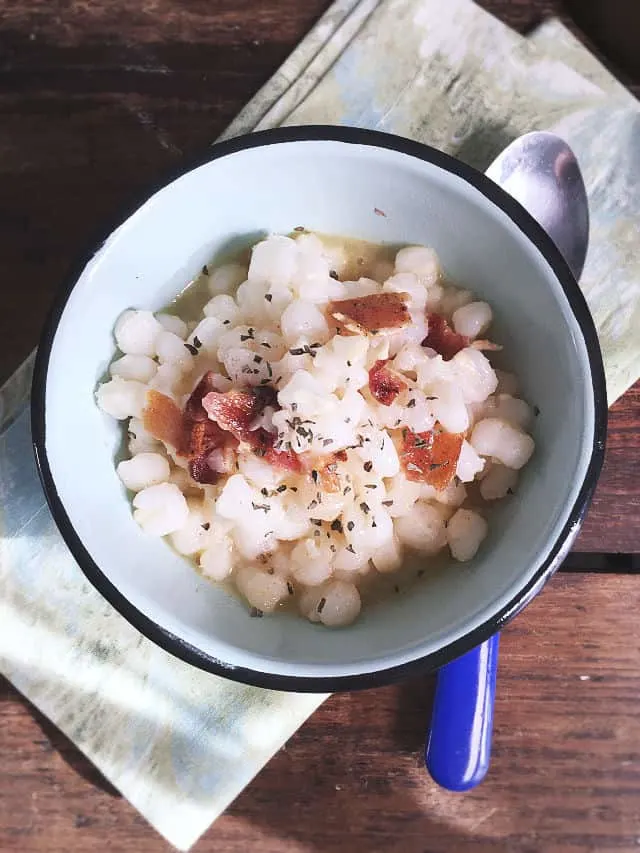 A bowl of hominy with blue handled spoon on green napkin from above