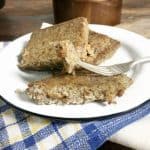 a fork holding a piece of scrapple with two other slices on a white plate