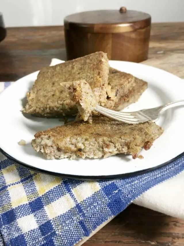 a fork holding a piece of scrapple with two other slices on a white plate