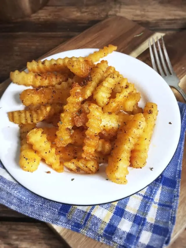 Golden crinkley fries on a white plate with blue napkin